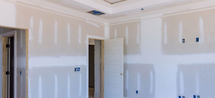 Interior of a room under construction showing unfinished drywall and a sophisticated ceiling design with multiple layers and recessed lighting placements.