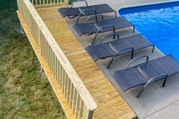 Overlooking a poolside, a new wooden deck with railings and lounging chairs, ideal for summer relaxation and outdoor enjoyment.