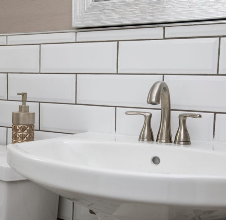 A minimalist bathroom featuring a clean white sink with modern faucet, set against classic white subway tiles and simple decor elements.